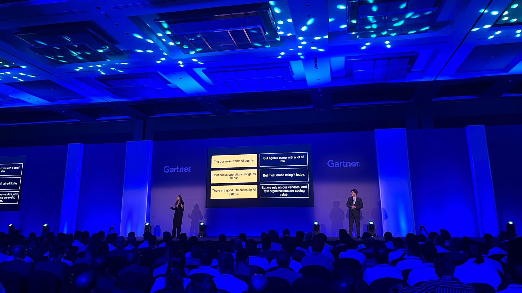 Two presenters on a Gartner conference stage before a keynote audience in a blue-lit ballroom.