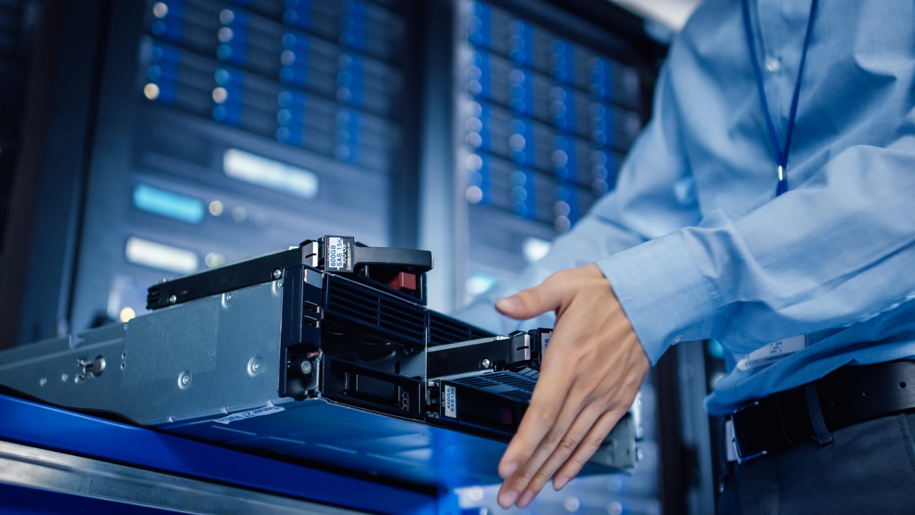 Technician handling labeled SAS drive caddies partially extracted from a rack server.