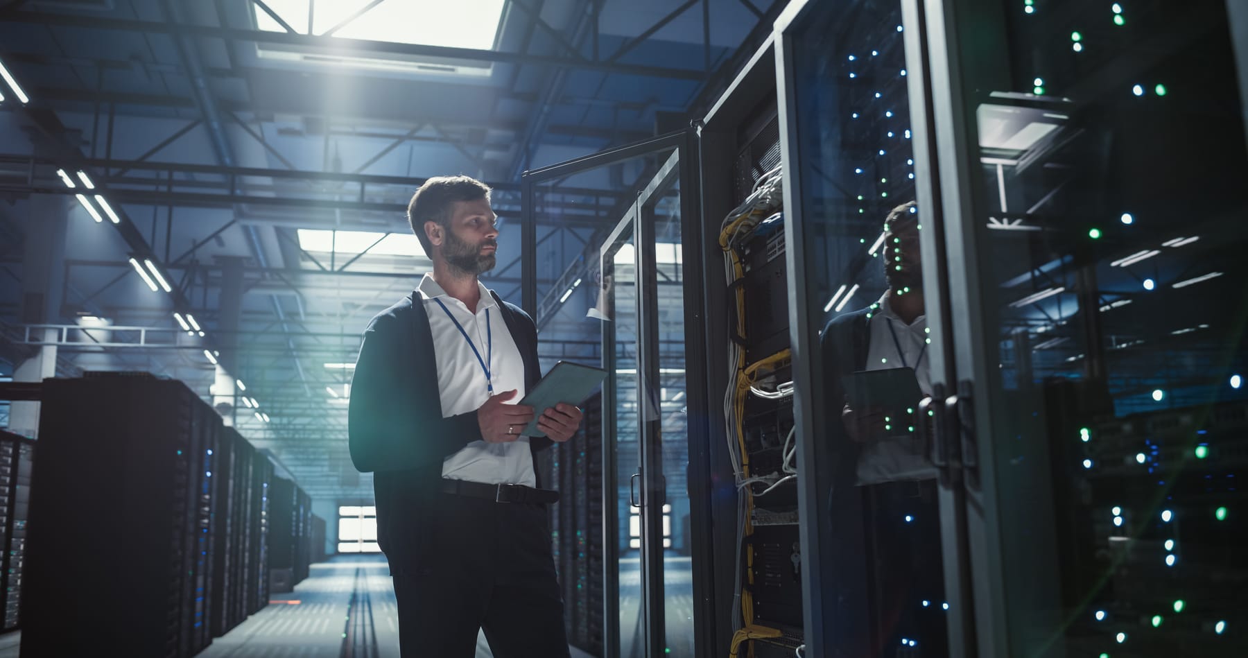 Engineer with a tablet standing at an open server rack door in a large data center.