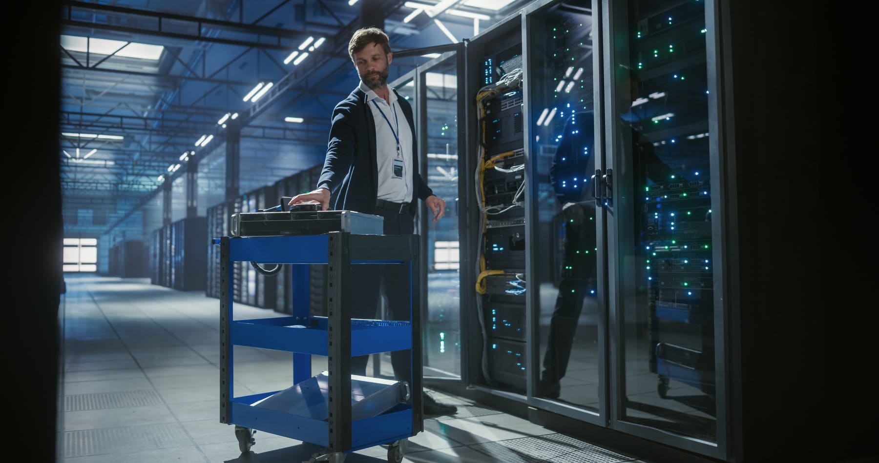 Engineer with a tool cart in front of an open rack with amber patch cabling in a data hall.